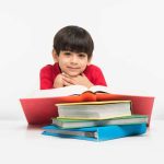 cute-little-indian-asian-boy-holding-reading-book-study-table-white-floor-isolated-white-background