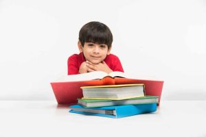 cute-little-indian-asian-boy-holding-reading-book-study-table-white-floor-isolated-white-background